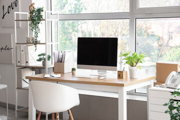 Blank computer monitor with folders and plants near window in office