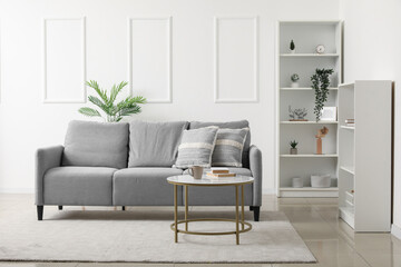 Interior of light living room with grey sofa, table and shelf units