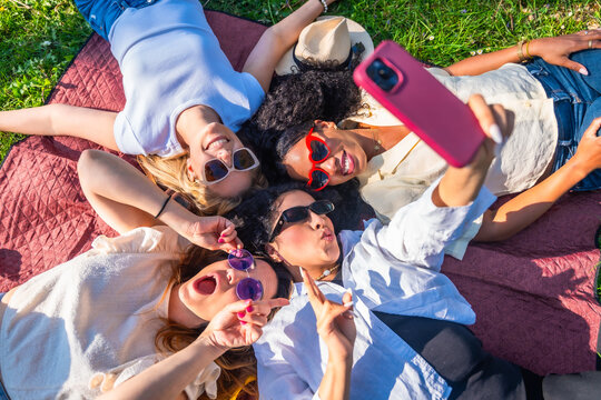 Four playful women taking a selfie lying on blanket in park