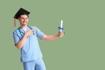 Happy male medical graduate with stethoscope pointing at diploma on green background