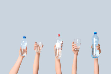 Female hands with bottles and glasses of water against grey background