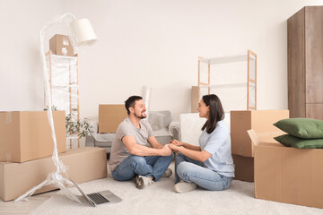 Young couple holding hands on carpet in their new flat