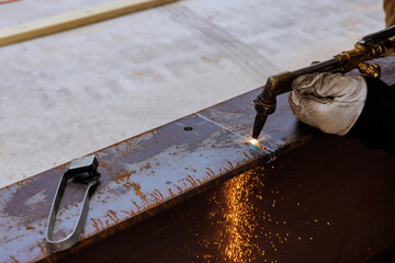 Worker carefully cuts metal using welding torch, creating sparks in busy industrial location under works day