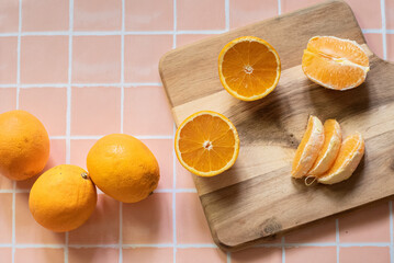Close-up of a hand holding a halved orange. In the background, sliced oranges rest on a wooden...