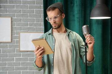 Male standup comedian with notebook and microphone performing on stage