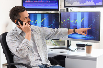 Male trader talking by mobile phone at table in office