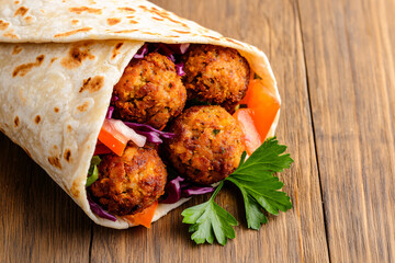 Fresh falafel wrap with red cabbage, tomatoes, and parsley served on a wooden table close-up.