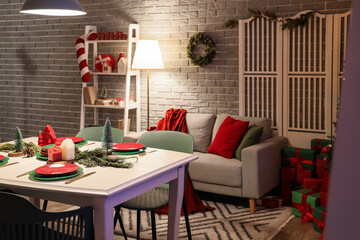 Interior of dining room decorated for Christmas with table, sofa and glowing lamps