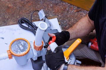 Contractor works diligently on pool pump, adjusting components at well lit outdoor works