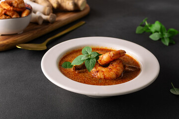 Fresh aromatic hot Thai soup Tom Yum with mushrooms, shrimps and different spices on black stone...