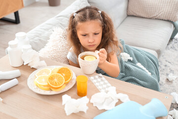 Sick little girl with sore throat taking cup of lemon tea from shelf at home