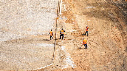 Aerial top view of construction workers in orange reflective vests shoveling sand at an urban...