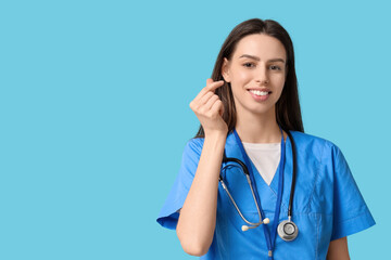 Young female doctor making heart gesture on blue background