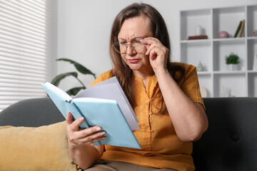 Woman with vision problem reading book on sofa at home