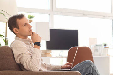 Thoughtful businessman working with laptop in armchair at office