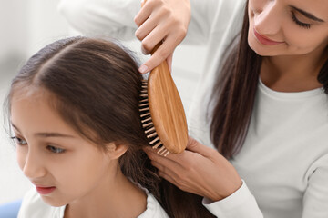 Naklejka premium Young mother brushing hair of her little daughter in bathroom, closeup