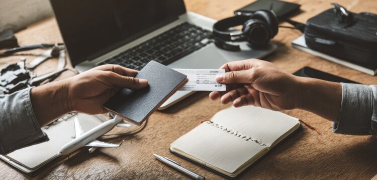 Passport and ticket exchange for global journeys. Hands on desk with laptop, headphones, and airplane model, symbolizing detailed travel planning and adventure preparation.