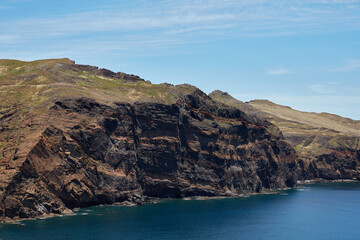 Fototapeta premium Dramatic rugged coastal cliffs towering over the deep blue ocean under a clear sky with hikers on a trail