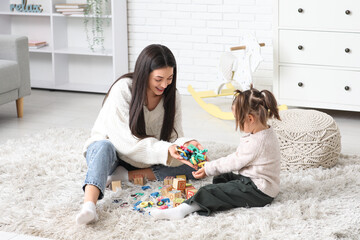 Cute little girl with teacher and letters learning alphabet on carpet at home
