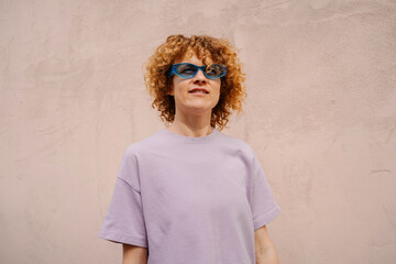 Woman in lilac t-shirt and blue sunglasses near pink wall