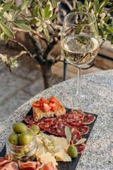 Outdoor dining or aperitif white wine glasses on a stone table with gourmet charcuterie board assorted meats, olives, and cheese