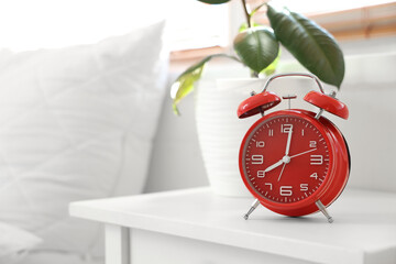 Red alarm clock and plant on table in bedroom, closeup