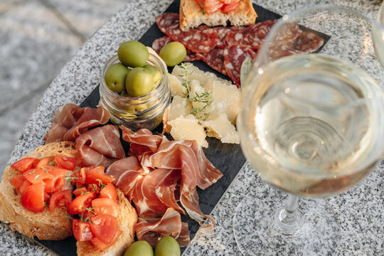 Gourmet charcuterie board with meats prosciutto ham, salami, green olives and cheese with white wine or prosecco aperitif or dinning outdoor Italian style - Powered by Adobe