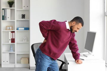 Young man suffering from back pain near table in office