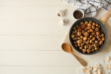 Frying pan with roasted mushrooms, garlic and bowl of peppercorns on white wooden background