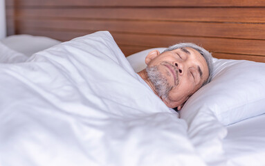 senior man laying comfortable under a white blanket,resting,bedtime deep sleeping in a cozy...