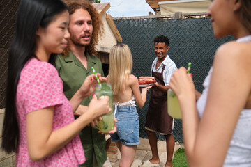 Diverse group of friends having fun at a barbecue party, drinking cocktails and eating grilled sausages