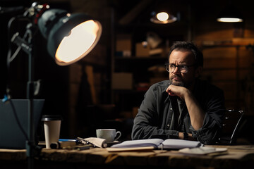 Creative studio vibes. Man deep in thought at  moody workspace with warm lighting, papers, coffee, quiet atmosphere. Perfect for stories about artists, content creators, or behind-the-scene moments.