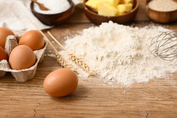 Heap of flour with eggs and wheat spikelets for preparing dough on wooden background