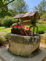 Old stone well with a small wooden roof and a flower box of red geraniums on the edge, evoking rustic charm and countryside life