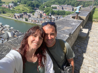 Happy couple taking a selfie on the balcony of Dinant citadel, with panoramic view of the city and Meuse River in the background.