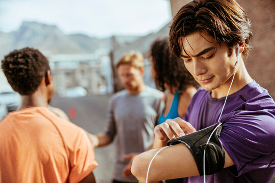 Young asian man using a smart phone before going jogging and exercising with his diverse group of friends