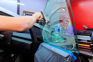 Worker cleans car window in workshop, applying detergent with squeegee for spotless finish during...