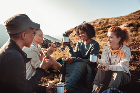 Young diverse group of female friends having a coffee break after hiking in the hills and mountains