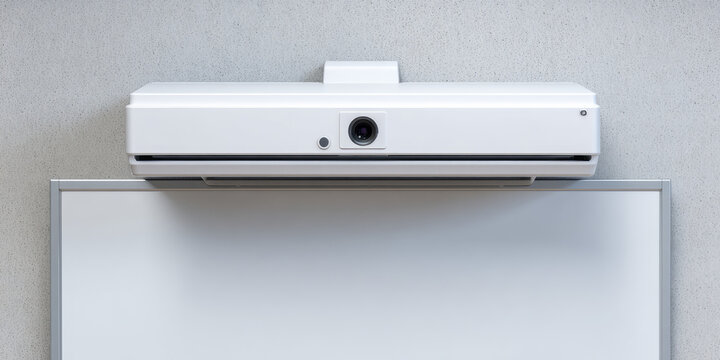 A white projector is mounted above a screen on a wall, ready for presentations. Conference equipment setup