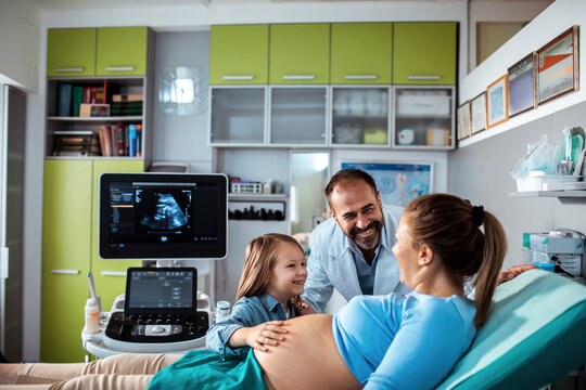 Pregnant woman at ultrasound appointment with daughter and smiling doctor