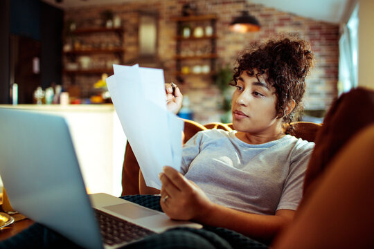 Young woman reviewing documents while working from home on laptop