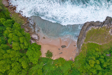 Drone shot of hidden beach, granite stones, wavy ocean, vegetation near the waterline, Mahe,...