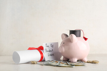 Paper with text PAY OFF STUDENT LOANS, piggy bank, degree and money on light table