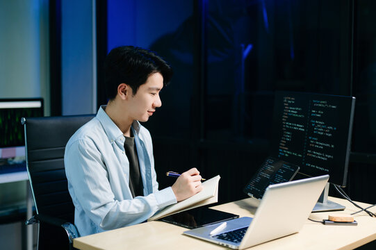 Young male programmer working with tablet and screen displaying code. Modern tech office setup, great for software