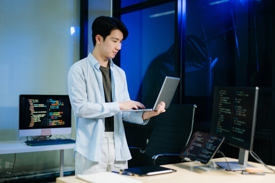 Young male programmer working with tablet and screen displaying code. Modern tech office setup, great for software