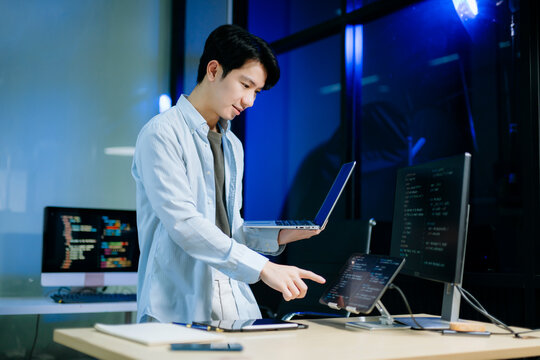 Asian software developer working late with code on screens, tablet, and phone. Concept of programming, tech lifestyle,