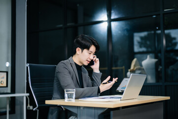 Obraz premium Confident young Asian businessman analyzing financial charts on laptop. Perfect for stock themes in business, finance