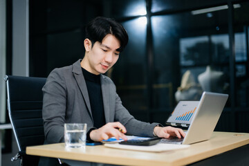 Confident young Asian businessman analyzing financial charts on laptop. Perfect for stock themes in business, finance