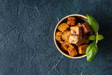 Bowl with pieces of fried tofu cheese and basil on dark background