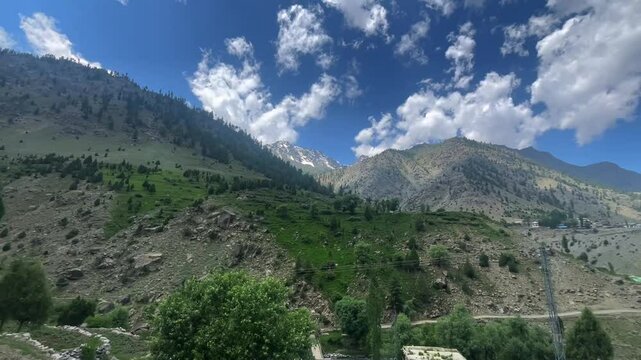 A peaceful valley view featuring crystal-clear blue river flowing between mountains, with a green village in sight. Blue sky with fluffy clouds enhances the serene atmosphere of this beautiful natural
